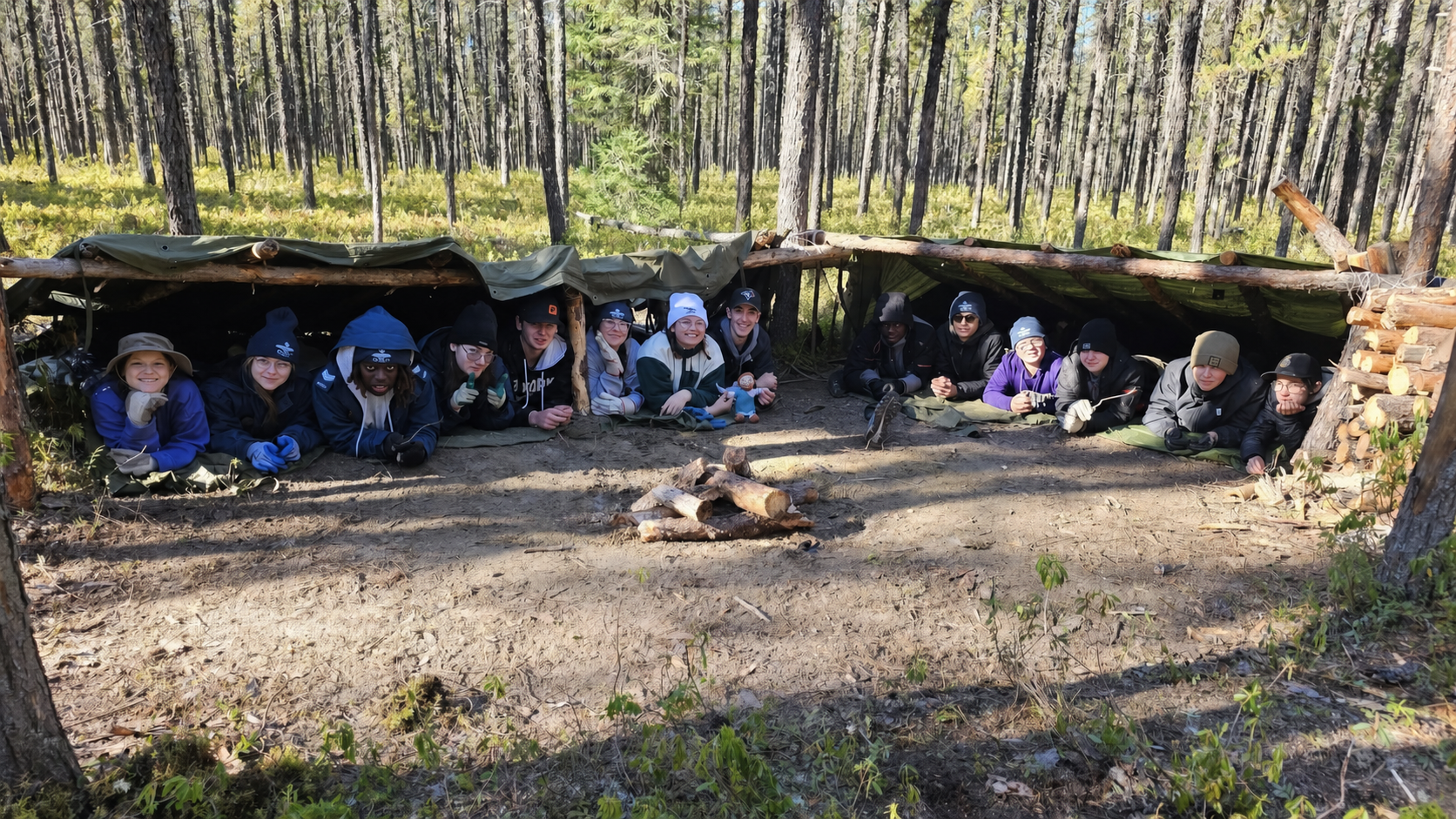 Des cadets de l’Escadron 839 réunis sous un abri de survie en forêt.